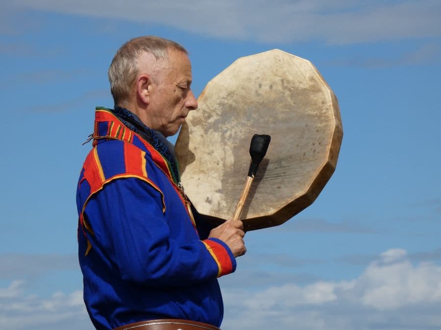The Sámi shaman strikes the frame drum, eyes closed