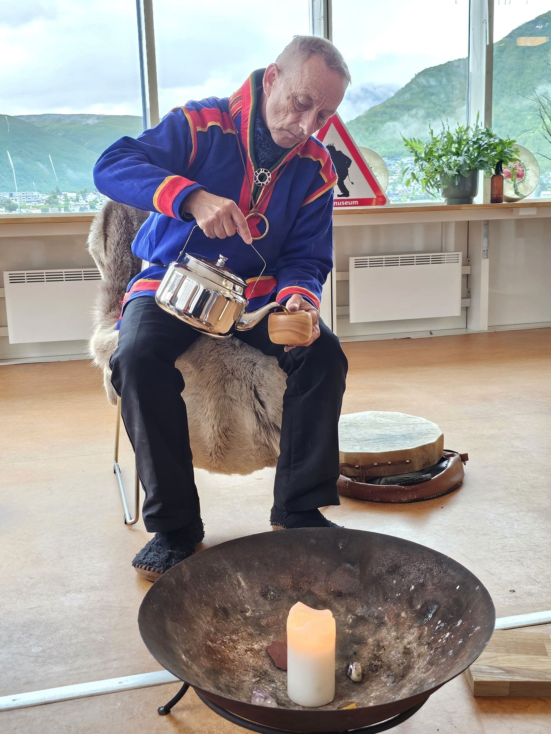 A Sámi shaman in traditional gákti pours coffee beside the fire bowl during the coffee ceremony