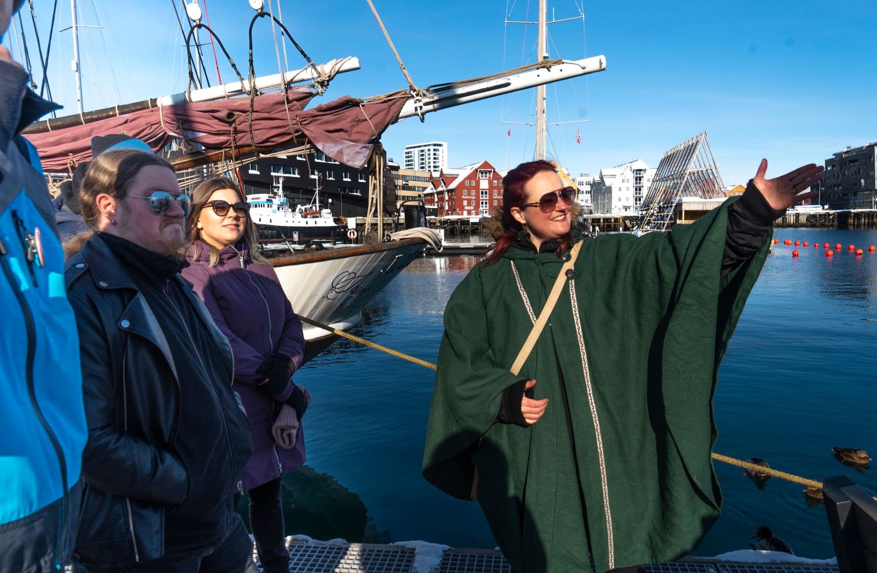 A guide in a green cape telling stories to guests on the Tromsø harbour front
